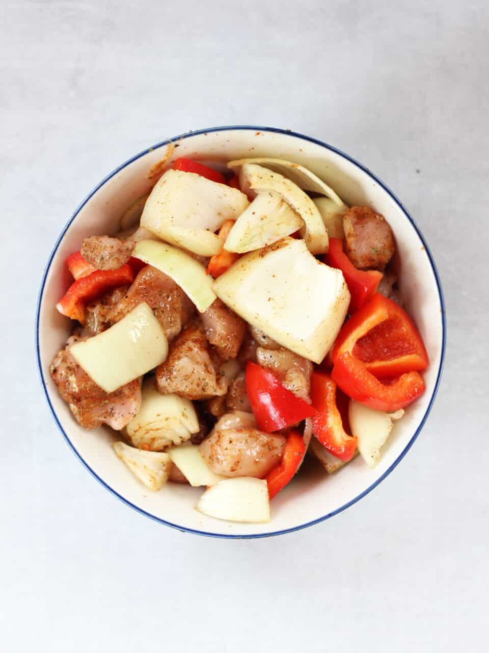 Skewer ingredients tossed in oil and seasonings in a bowl.