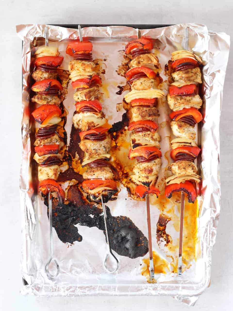 Oven baked chicken skewers on a foil lined tray.