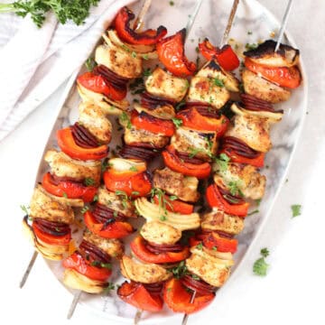 Chicken chorizo skewers on a serving plate with fresh parsley garnish.