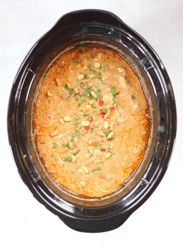 Chicken Panang curry in a slow cooker garnished with fresh cilantro, sliced red chilies and peanuts.