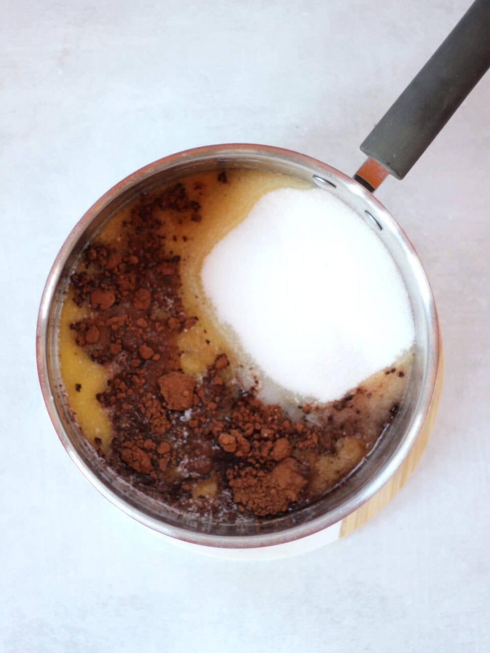 Sugar and cocoa powder added to melted butter in a pot.