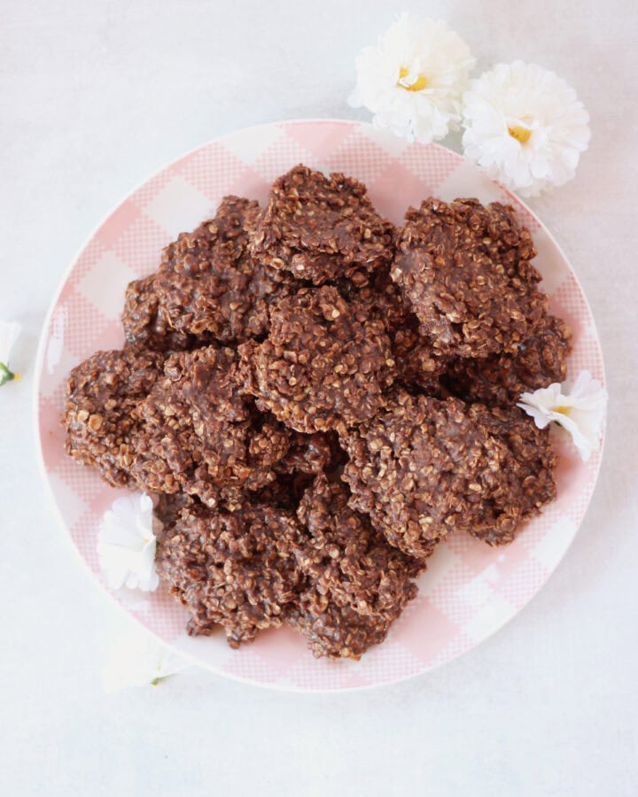 Chocolate cookies on a pink and white checked plate next to white flowers.