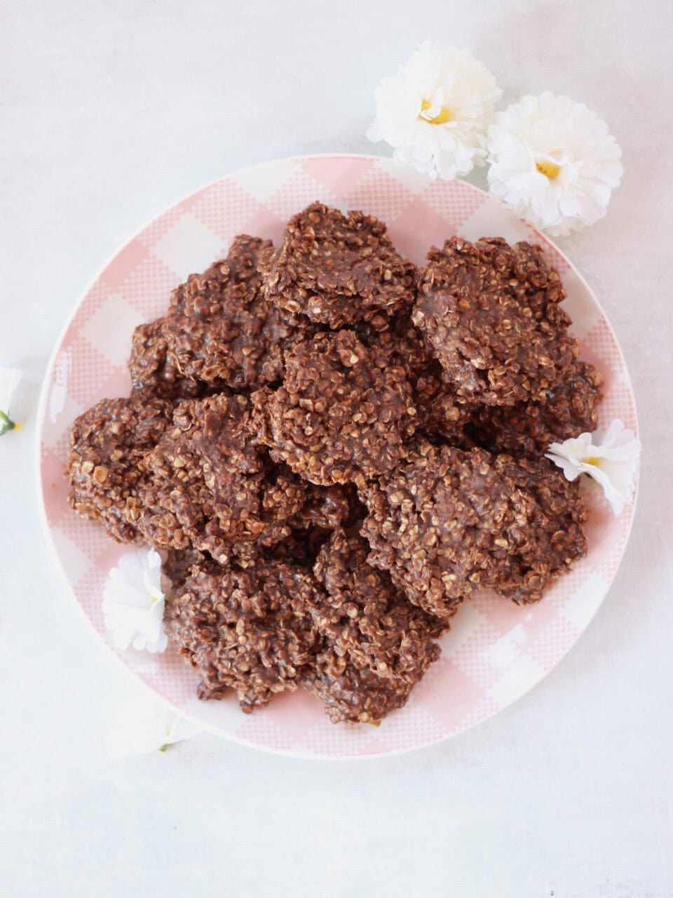 Chocolate cookies on a pink and white checked plate next to white flowers.
