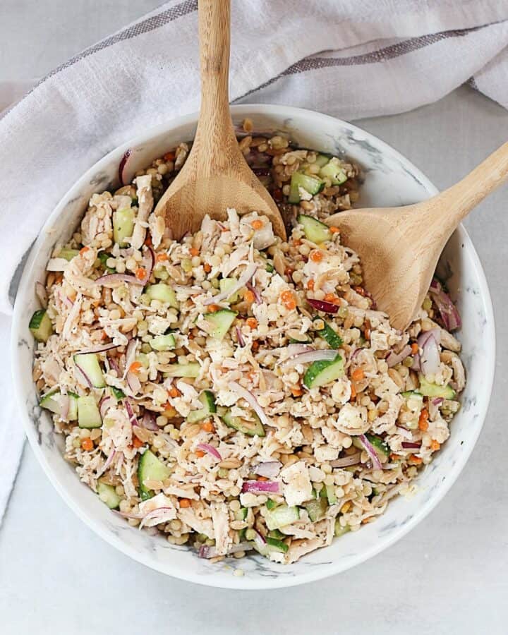 Pearl couscous and chicken salad served in a large bowl with wooden serving spoons.