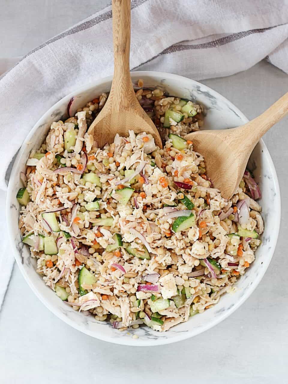 Pearl couscous and chicken salad served in a large bowl with wooden serving spoons.