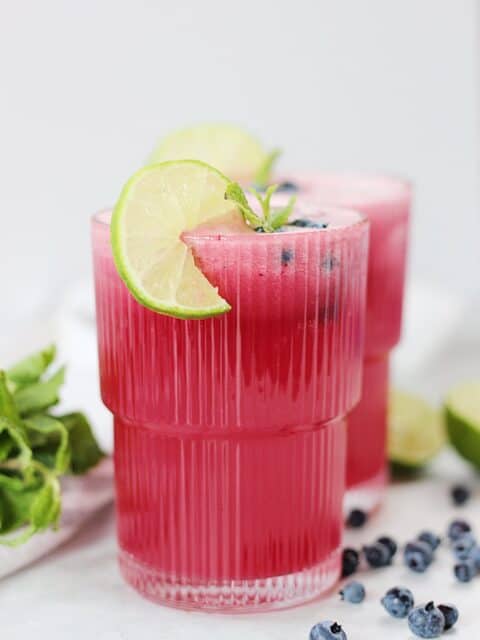 Blueberry limeade in a tall glass with lime and mint garnish.
