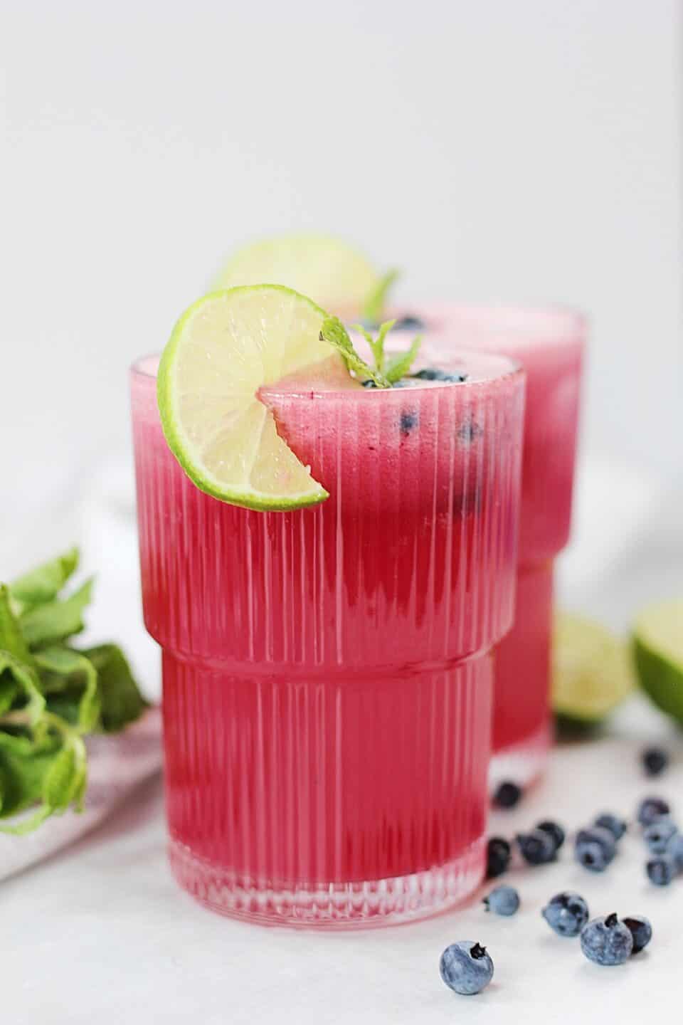 Blueberry limeade in a tall glass with lime and mint garnish.
