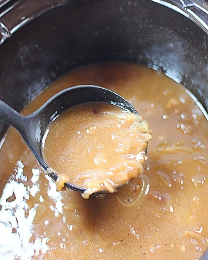 Onion gravy in a ladle in a slow cooker.