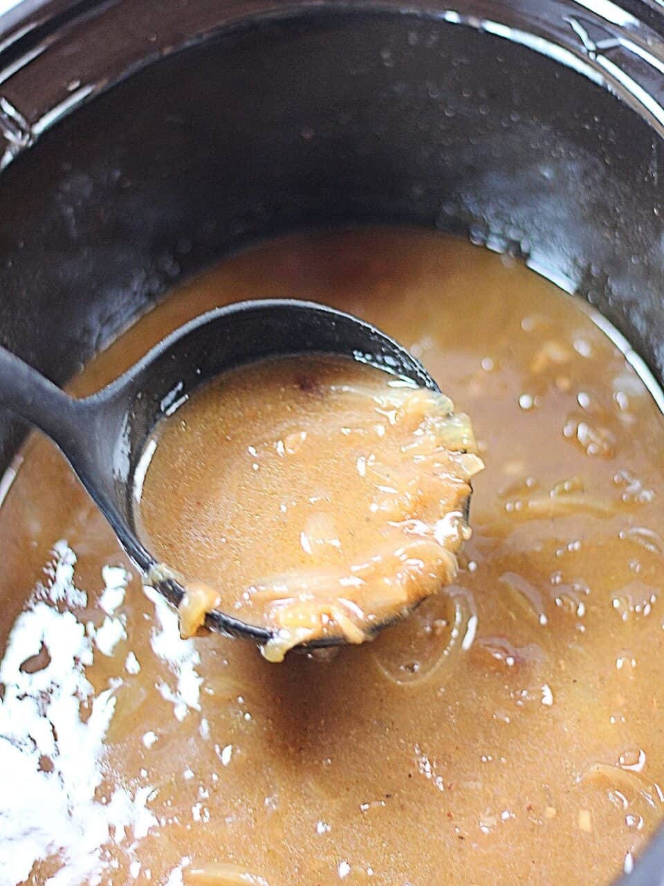 Onion gravy in a ladle in a slow cooker.