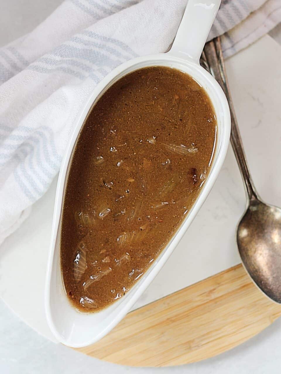 Rich onion gravy in a gravy boat next to a spoon.