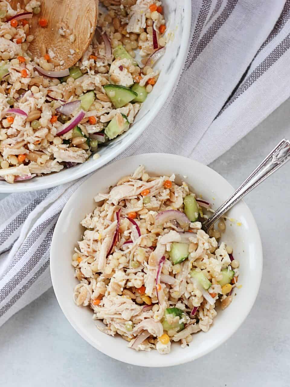 Shredded chicken couscous salad served in a small bowl with a fork.