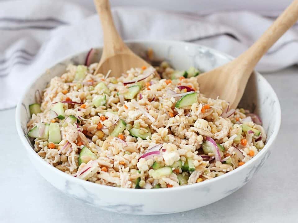 Israeli couscous salad in a large bowl with two wooden serving spoons.