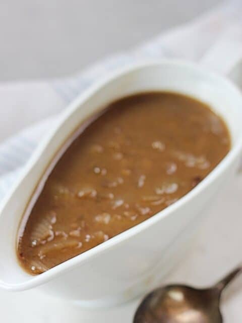 Gravy in a gravy boat next to a spoon.