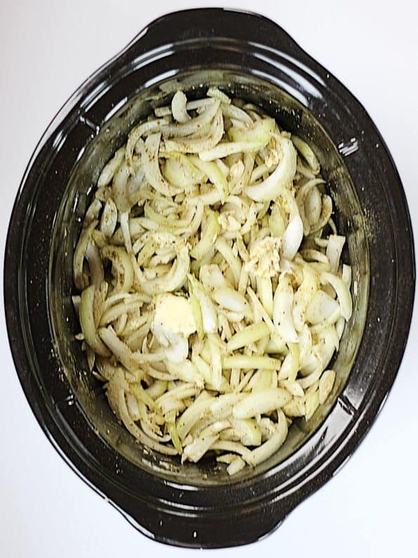 Sliced raw onions, butter and seasonings in a slow cooker.