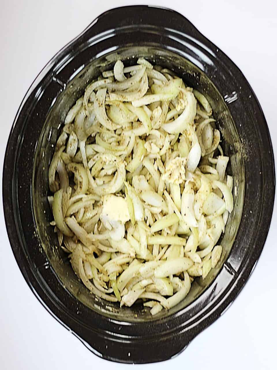 Sliced raw onions, butter and seasonings in a slow cooker.