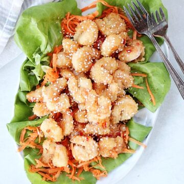 Crispy shrimp on a bed of lettuce and shredded carrots garnished with sesame seeds.