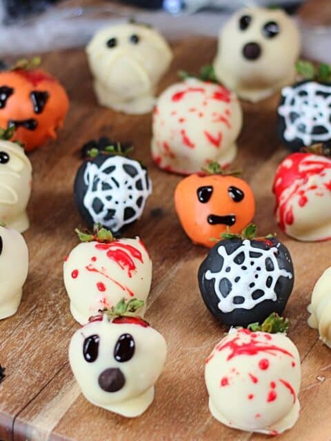 Chocolate covered Halloween strawberries on a wooden chopping board with Halloween decorations.