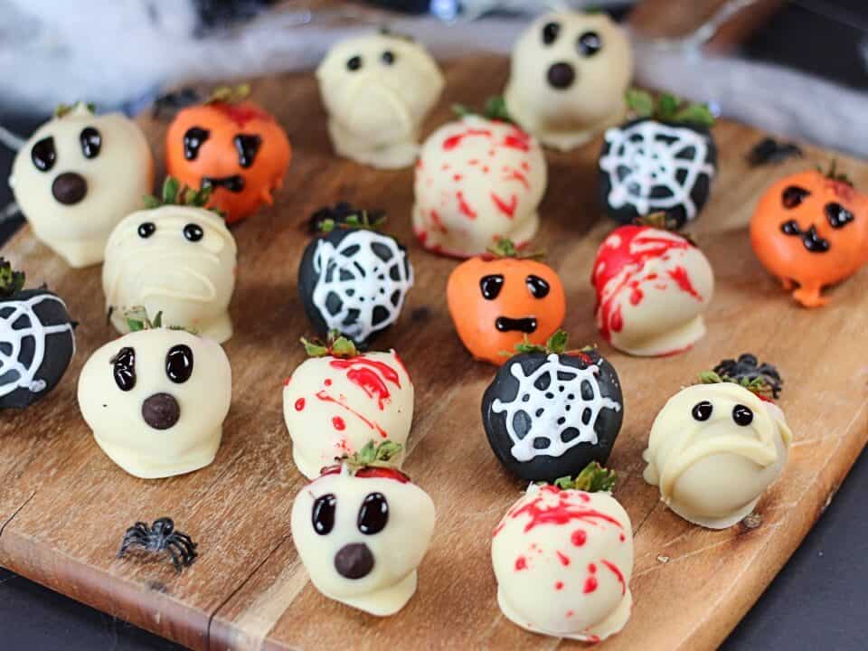 Chocolate covered Halloween strawberries on a wooden chopping board with Halloween decorations.