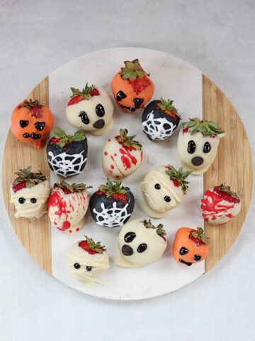 Halloween decorated chocolate covered strawberries on a round chopping board.