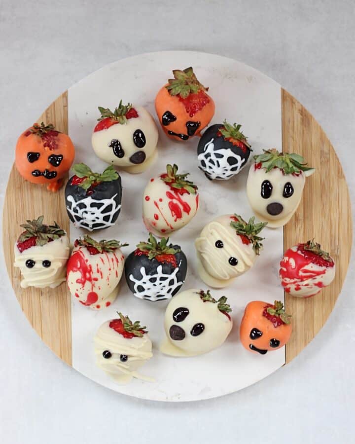 Halloween decorated chocolate covered strawberries on a round chopping board.