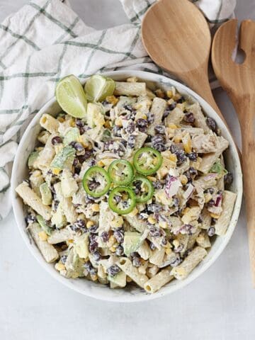 A bowl of Mexican pasta salad next to wooden salad servers.