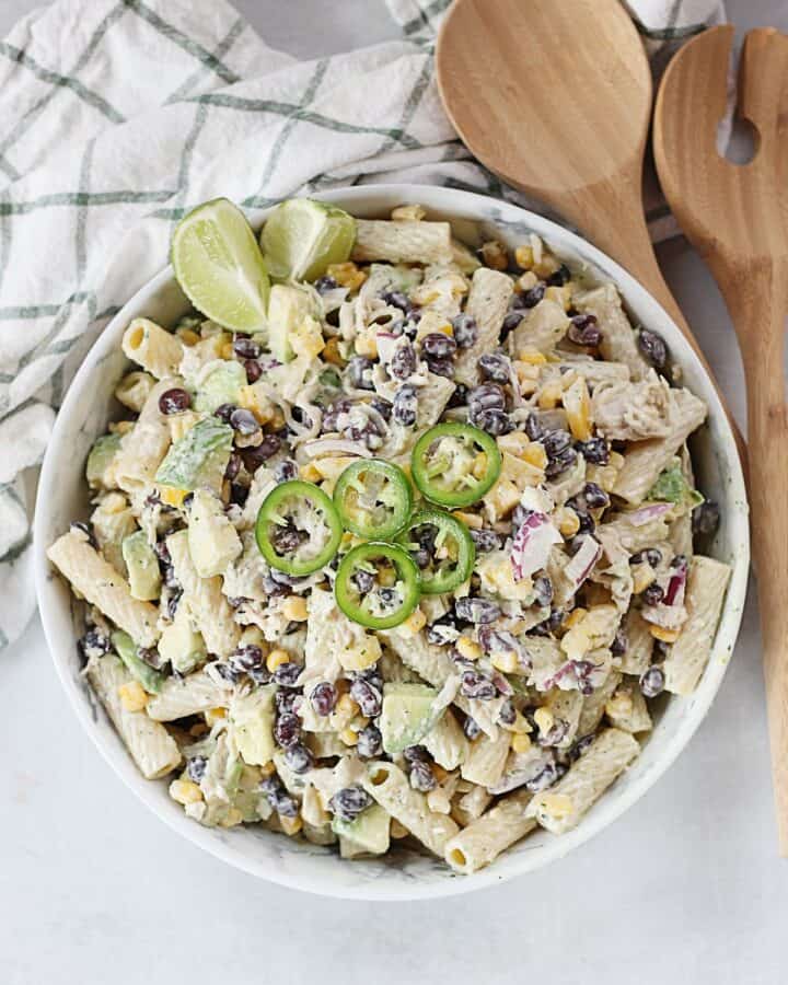 A bowl of Mexican pasta salad next to wooden salad servers.