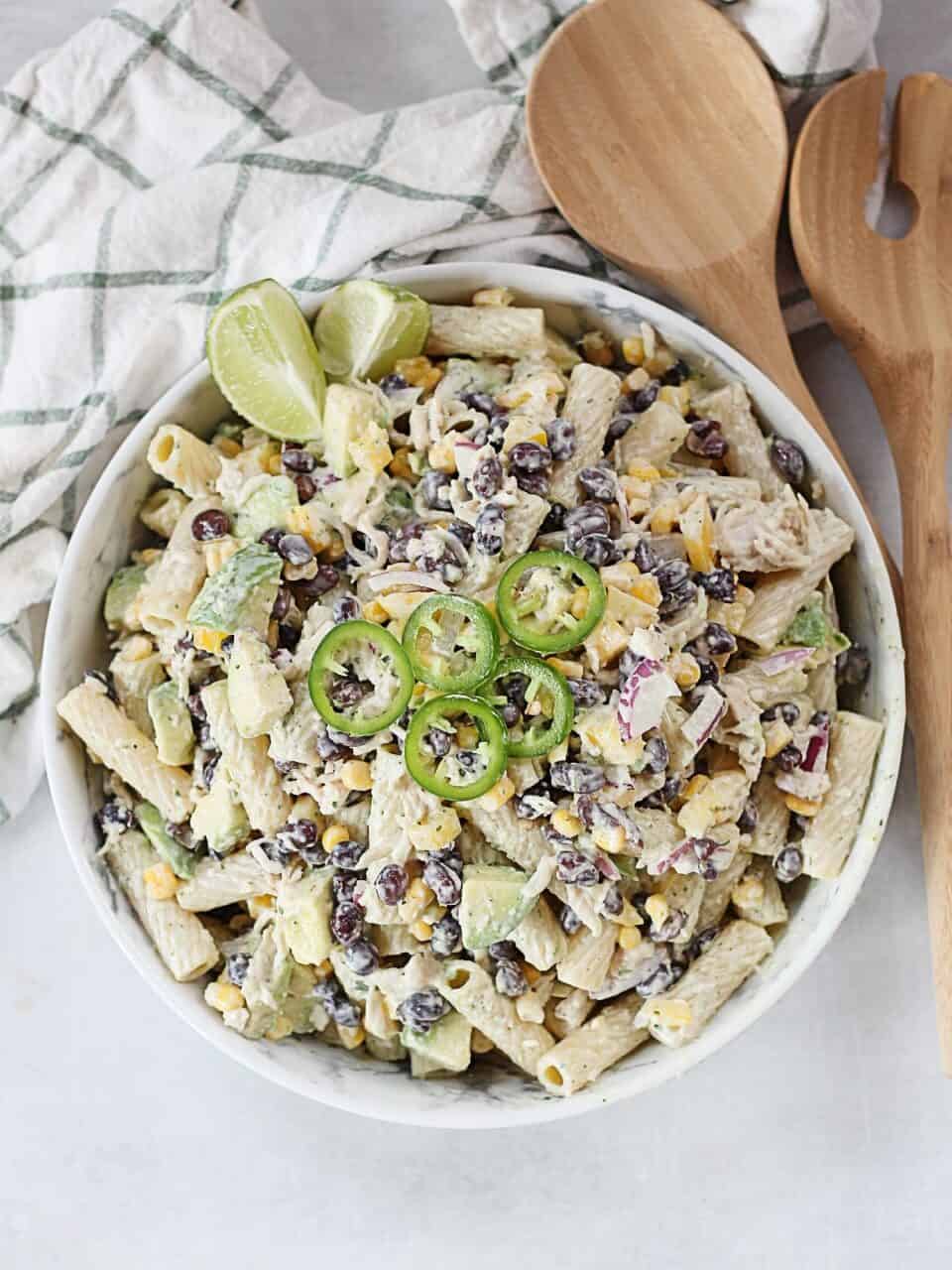 A bowl of Mexican pasta salad next to wooden salad servers.
