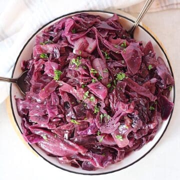 Slow cooker shredded red cabbage served in a white bowl with two spoons.