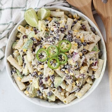 Mexican pasta salad served in a bowl garnished with lime wedges and sliced jalapenos.